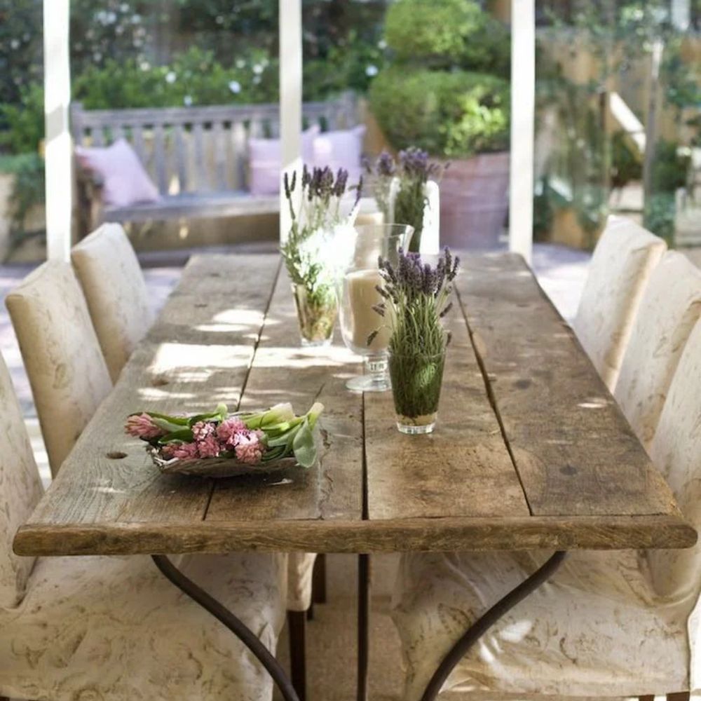 Rustic farmhouse dining table with lavender centerpieces and upholstered chairs in garden setting