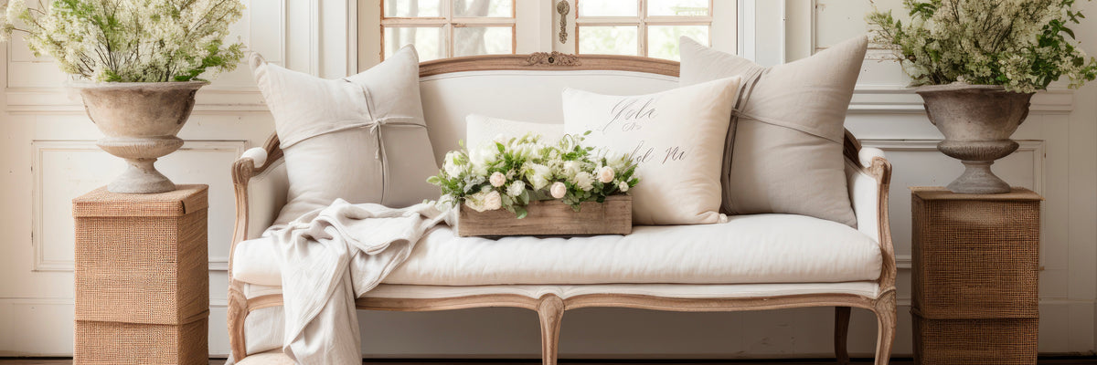French country style cream upholstered sofa with linen pillows and white floral arrangement.