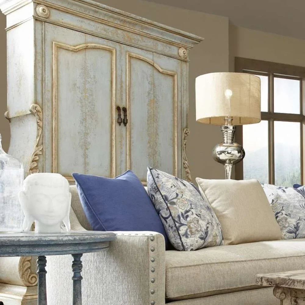 Shabby chic armoire with distressed finish, cozy sofa, and decorative pillows in French country style living room