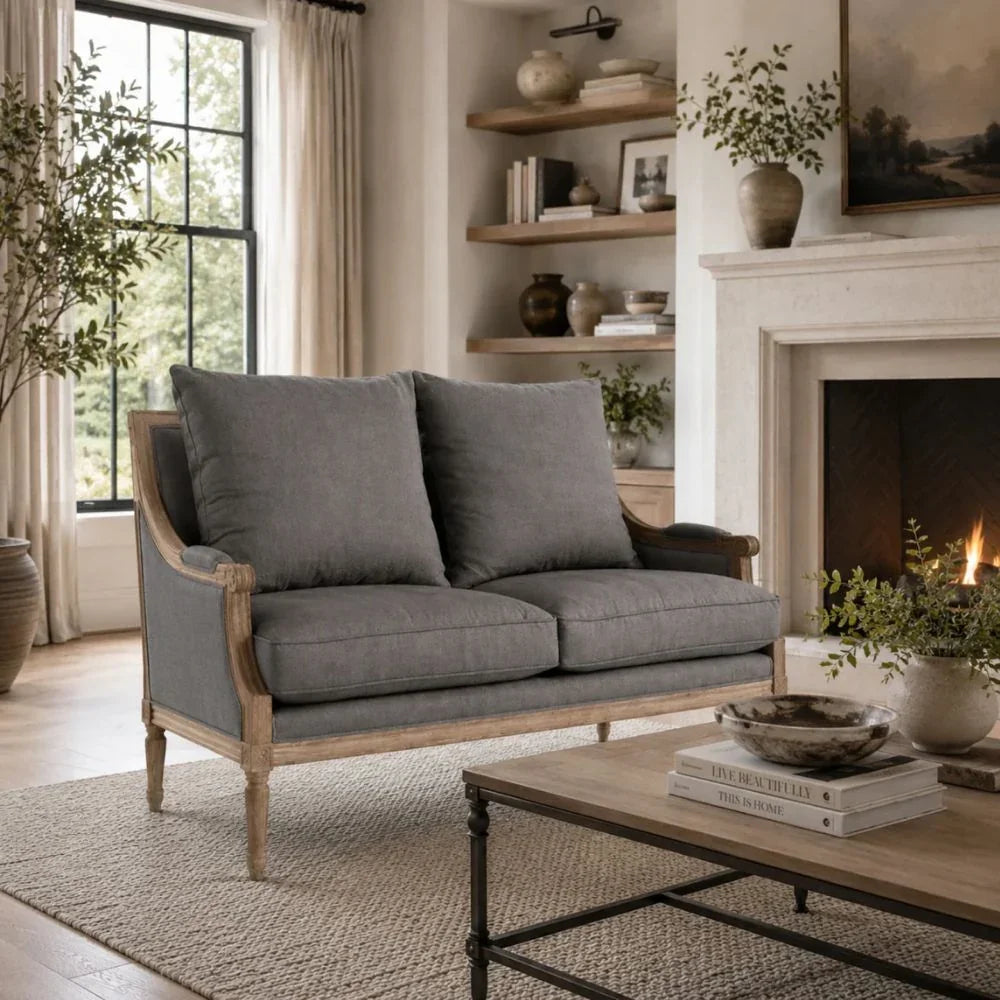 Gray French country loveseat with wooden frame in cozy living room with fireplace and shelves