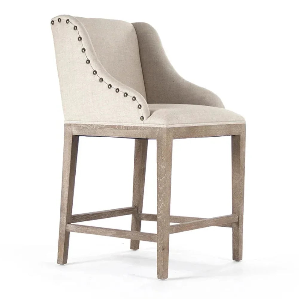 Farmhouse-style upholstered bar stool with nailhead trim and distressed wood legs
