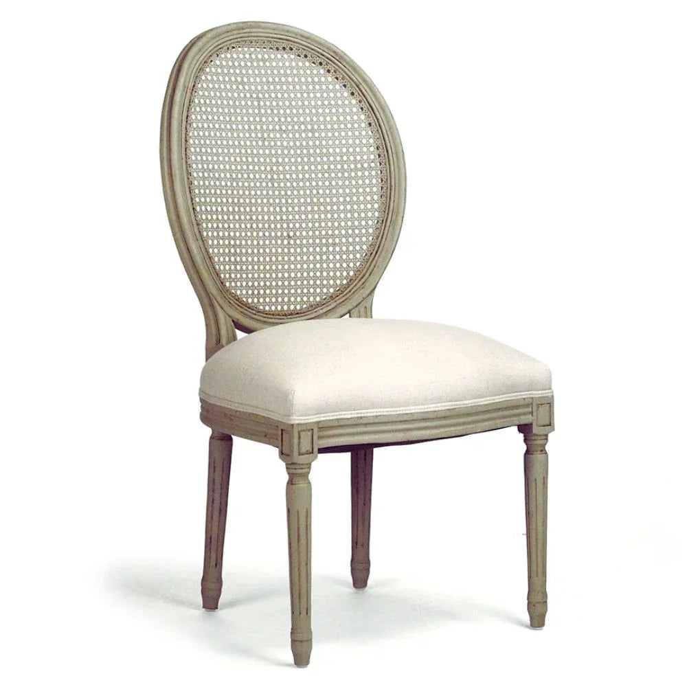 An elegant side chair with a distressed light gray wood frame, a round woven cane backrest, and a cream upholstered seat cushion, shown on a white background.
