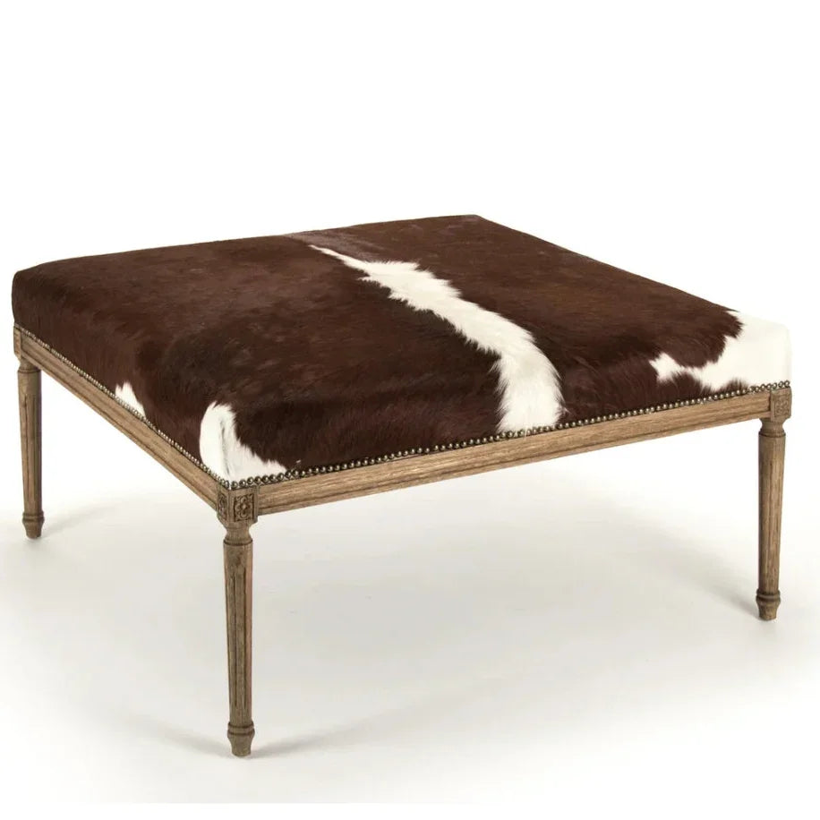 Brown and white cowhide upholstered square ottoman with nailhead trim and wooden legs.