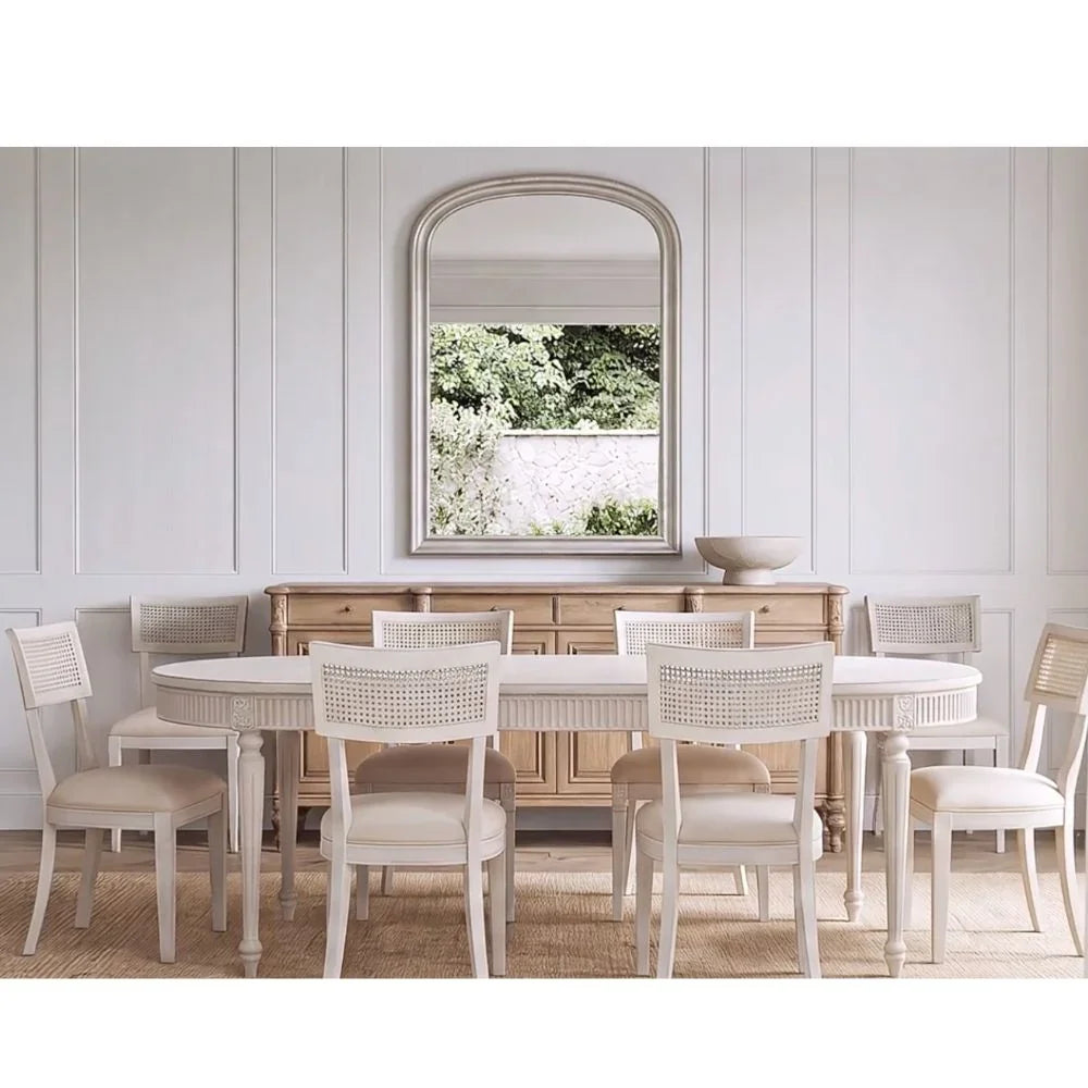 French country dining set with a white oval table and cane-back chairs in a neutral room.