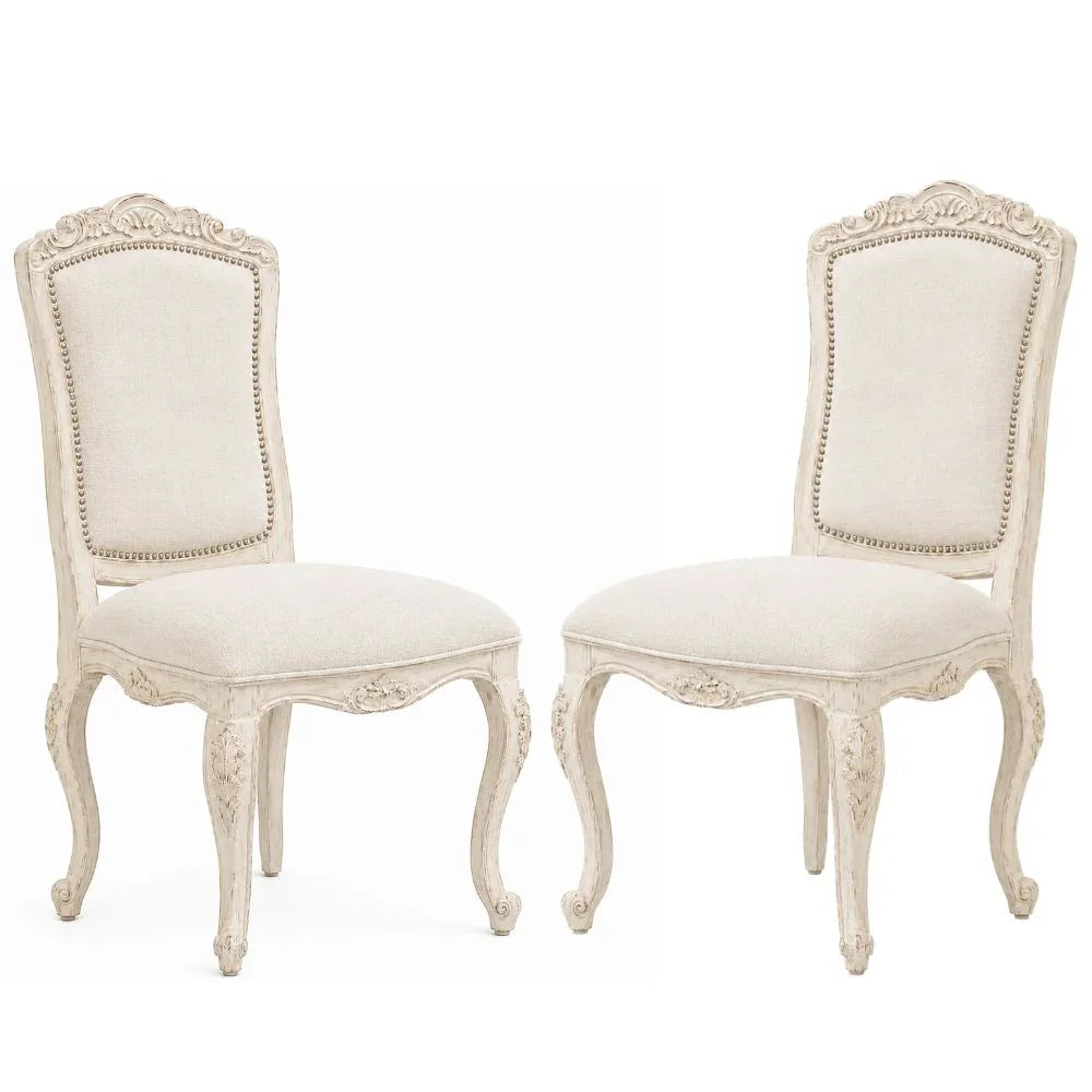 Elegant French country dining chairs with ornate carvings, distressed finish, and nailhead trim in cream fabric
