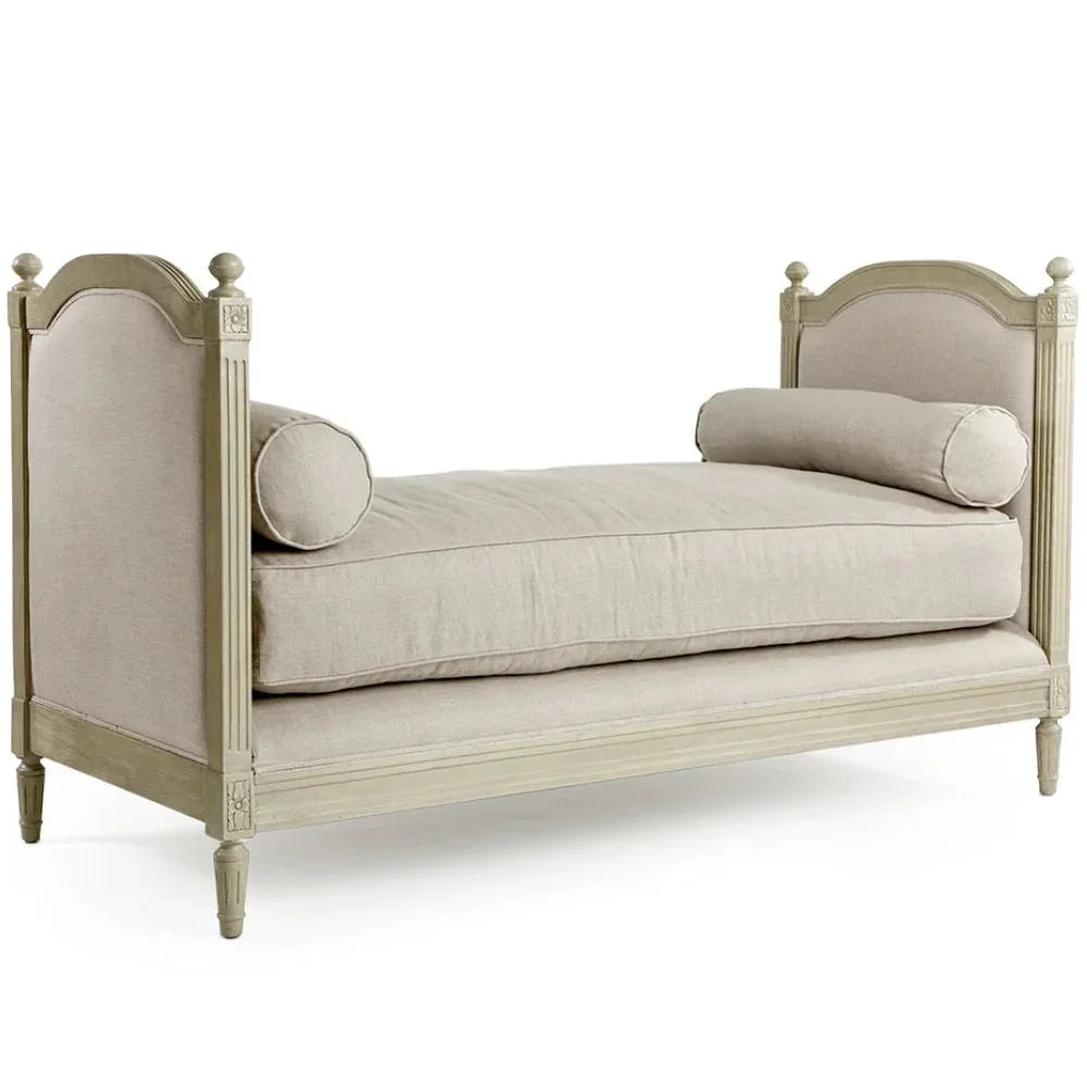 French country-style daybed with cream upholstery, rolled pillows, and carved wooden frame