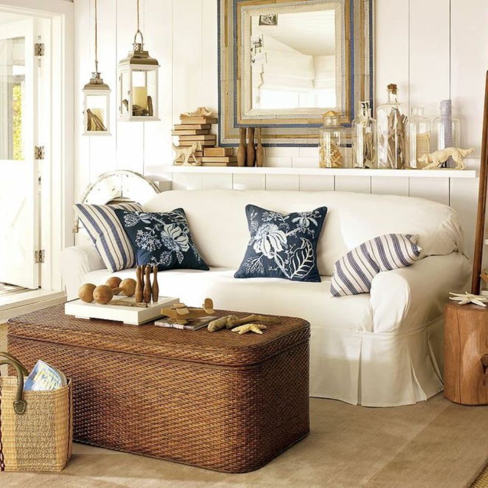Coastal-style white slipcovered sofa with navy floral pillows, wicker coffee table, and shabby chic decor