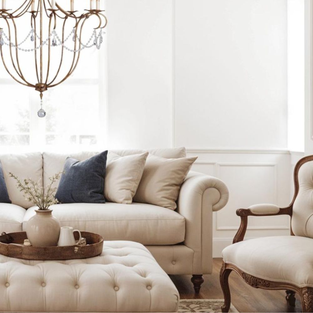 Elegant French country living room with cream sofa, tufted ottoman, and ornate chandelier