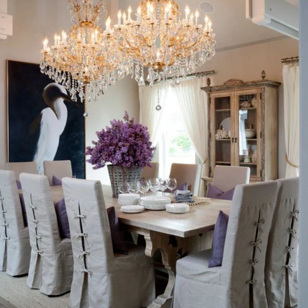 Elegant dining room with French country table, linen slipcovered chairs, crystal chandelier, and rustic hutch