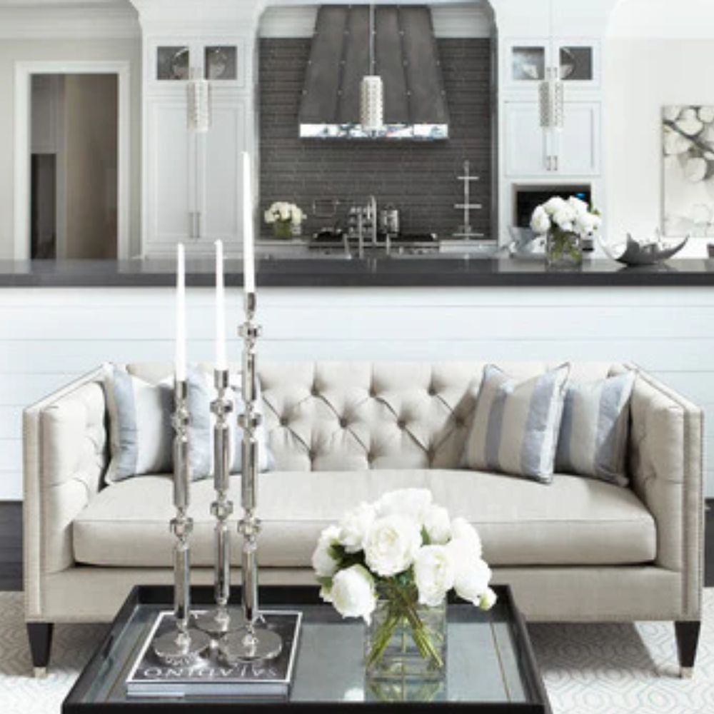 Tufted beige sofa with striped pillows in modern farmhouse living room, glass coffee table with white roses