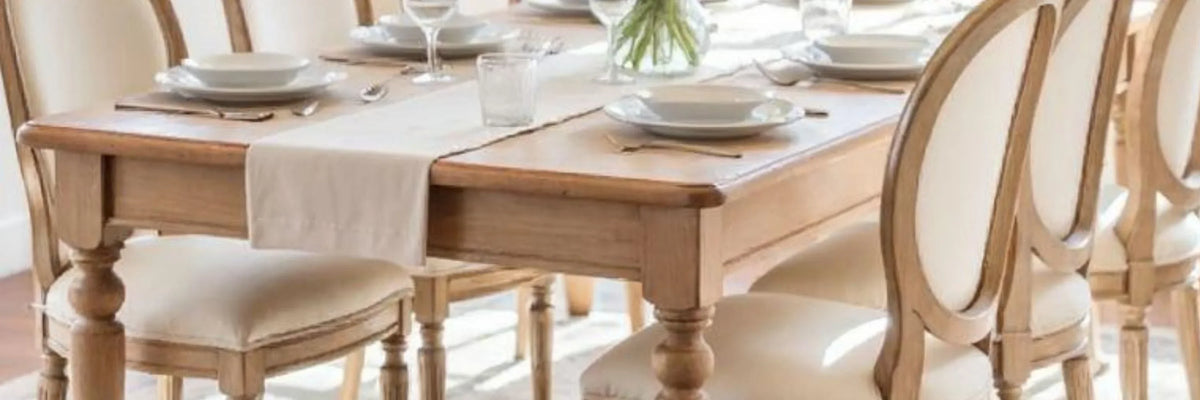 French country dining table with upholstered chairs, set for a meal in shabby chic style