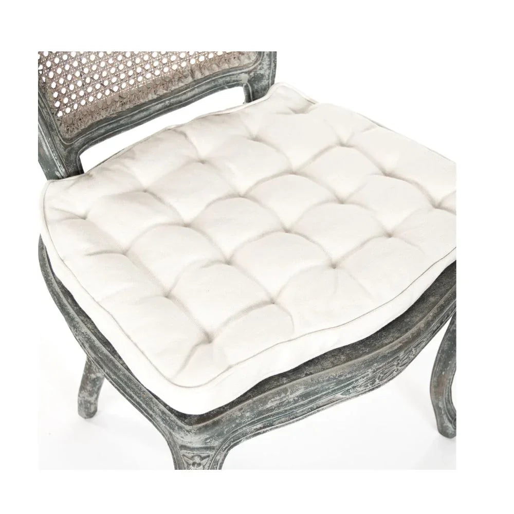 Cream tufted seat cushion on distressed French country cane chair with carved wood frame