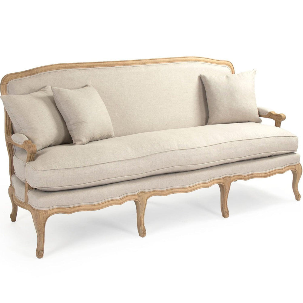 French country sofa with carved wood frame, neutral linen upholstery, and matching throw pillows