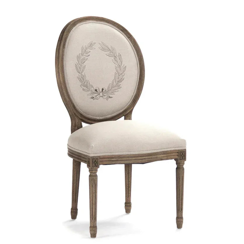 Elegant French country dining chair with embroidered laurel wreath, distressed wood frame, and neutral upholstery